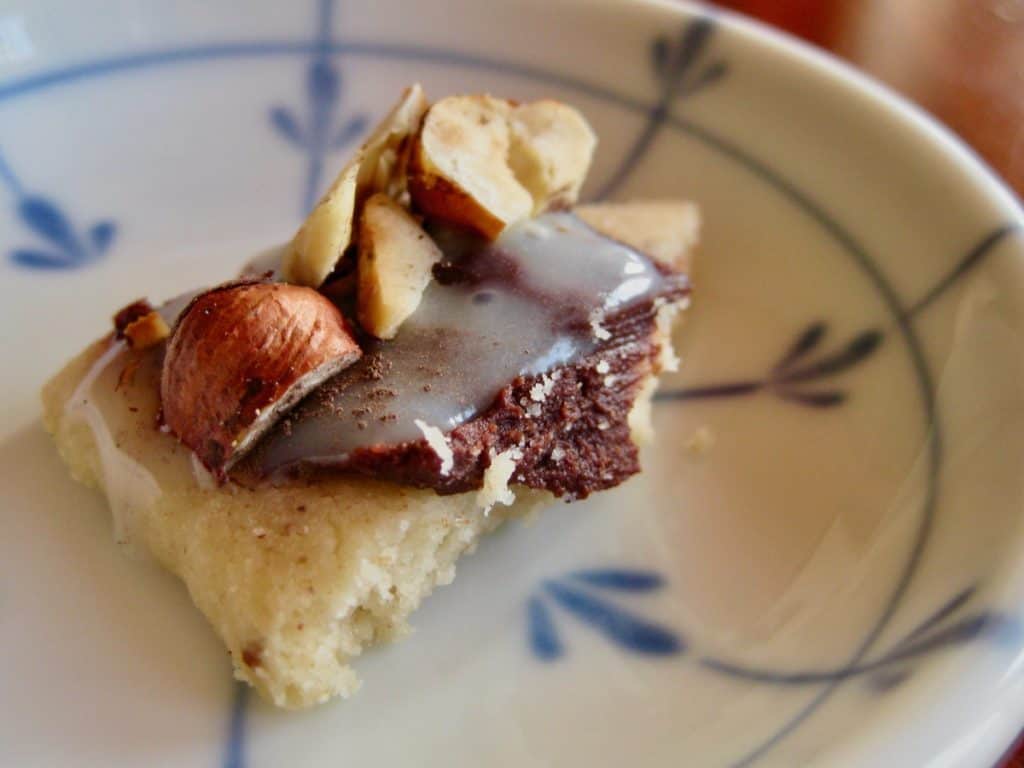 A bite of a Sugar Cookie topped with Chocolate Ganache, hazelnuts and White Chocolate Dipping Sauce.