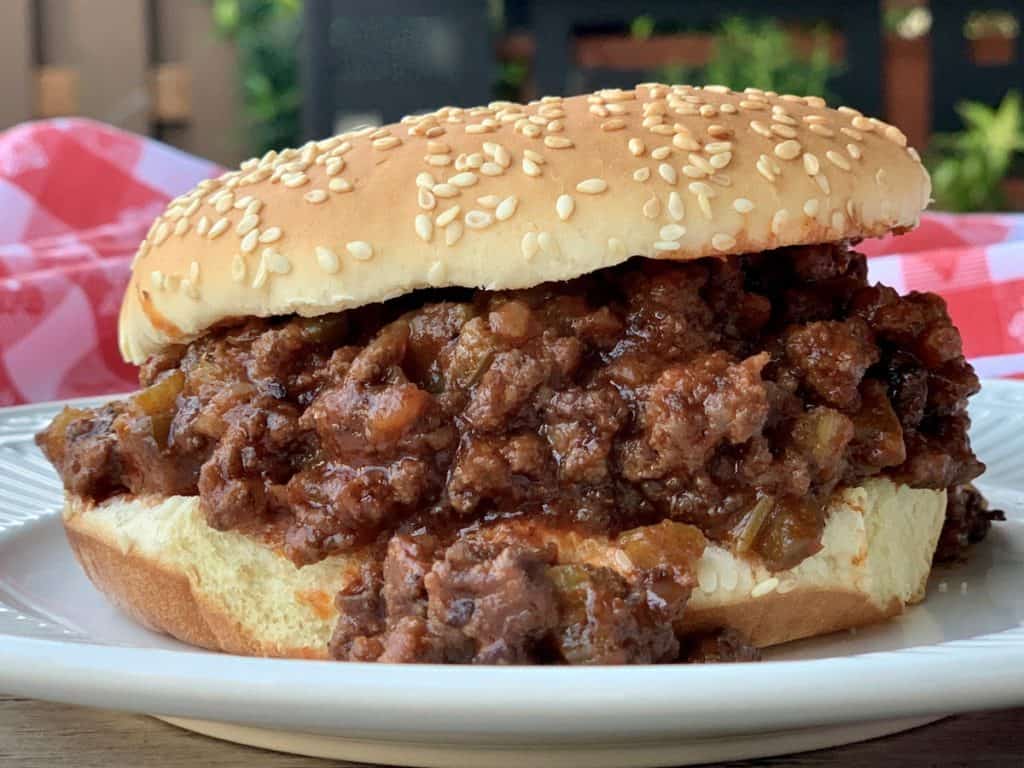 Mama Jean's Barbecue piled on a sesame seed hamburger bun with a checkered tablecloth in the background..