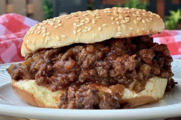 Mama Jean's Barbecue piled on a sesame seed hamburger bun with a checkered tablecloth in the background..