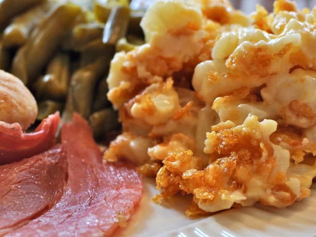 Buttered Cornflake Potato Casserole, made from hash brown potatoes, on a dinner plate beside a slice of Country Ham and a serving of Southern Style Green Beans.
