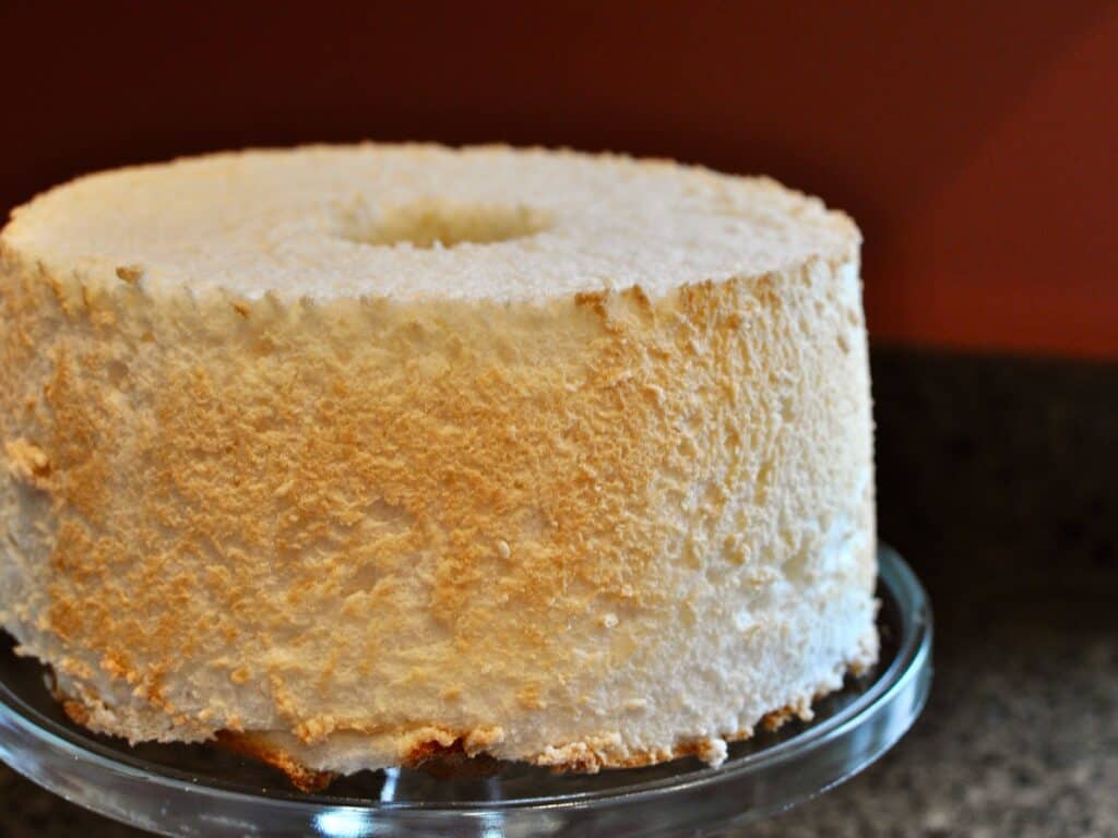 A freshly baked Angel Food Cake, just removed from the pan and resting on a cake stand.