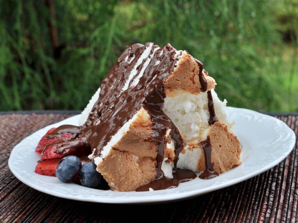 A slice of High Rise Angel Food Cake with berries, drizzled with chocolate ganache. 