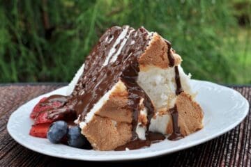 A slice of High Rise Angel Food Cake with berries, drizzled with chocolate ganache.