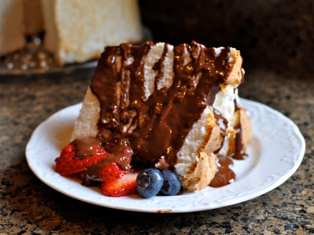 A slice of Angel Food Cake drizzled with chocolate and served with fresh berries.