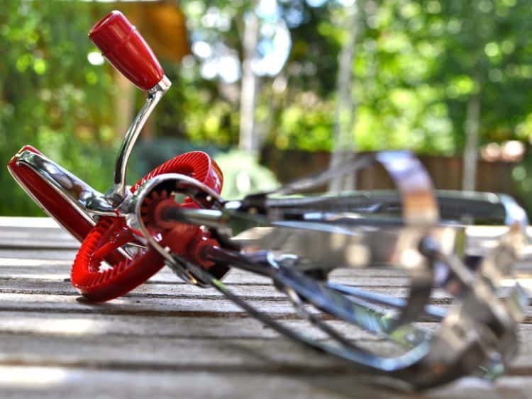 A hand-cranked mixer, or rotary egg beater, on a wooden table.