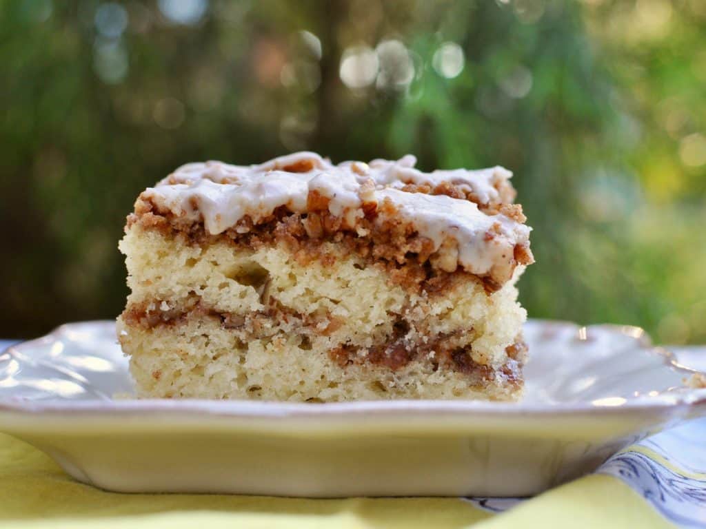 A slice of Pecan Graham Cracker Coffee Cake with a streusel topping served on a square plate in the garden.