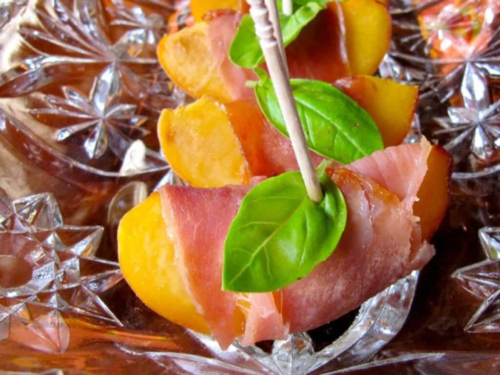 Nectarine Bites with Prosciutto and Basil are arranged on a glass tray.