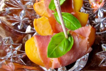 Nectarine Bites with Prosciutto and Basil are arranged on a glass tray.