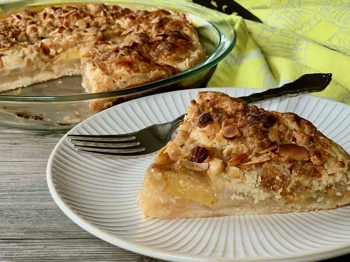 A slice of Ginger Pear Pie is served on a small plate with the cut pie in the background.