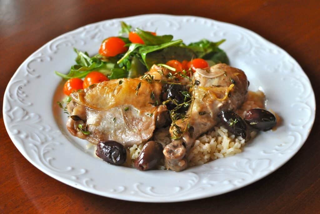 Roasted Chicken with Olives and Thyme is served over rice with a salad of arugula and cherry tomatoes.