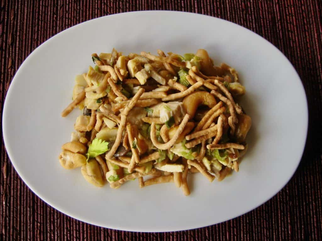 A serving of Cashew Chicken Casserole topped with chow mein noodles on an oval white plate, viewed from above.