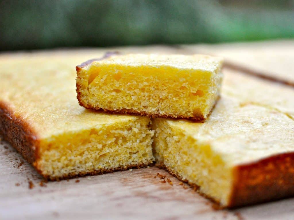 A slice of Cornbread for a Crowd stacked on top of a slab of cornbread sliced into serving sized pieces.