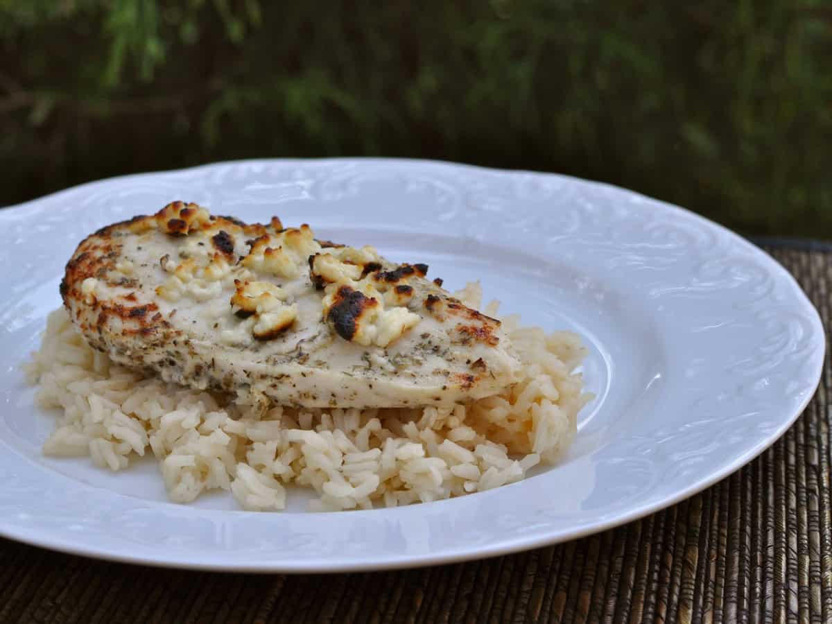 Greek Feta Chicken on a bed of rice served on a white plate.