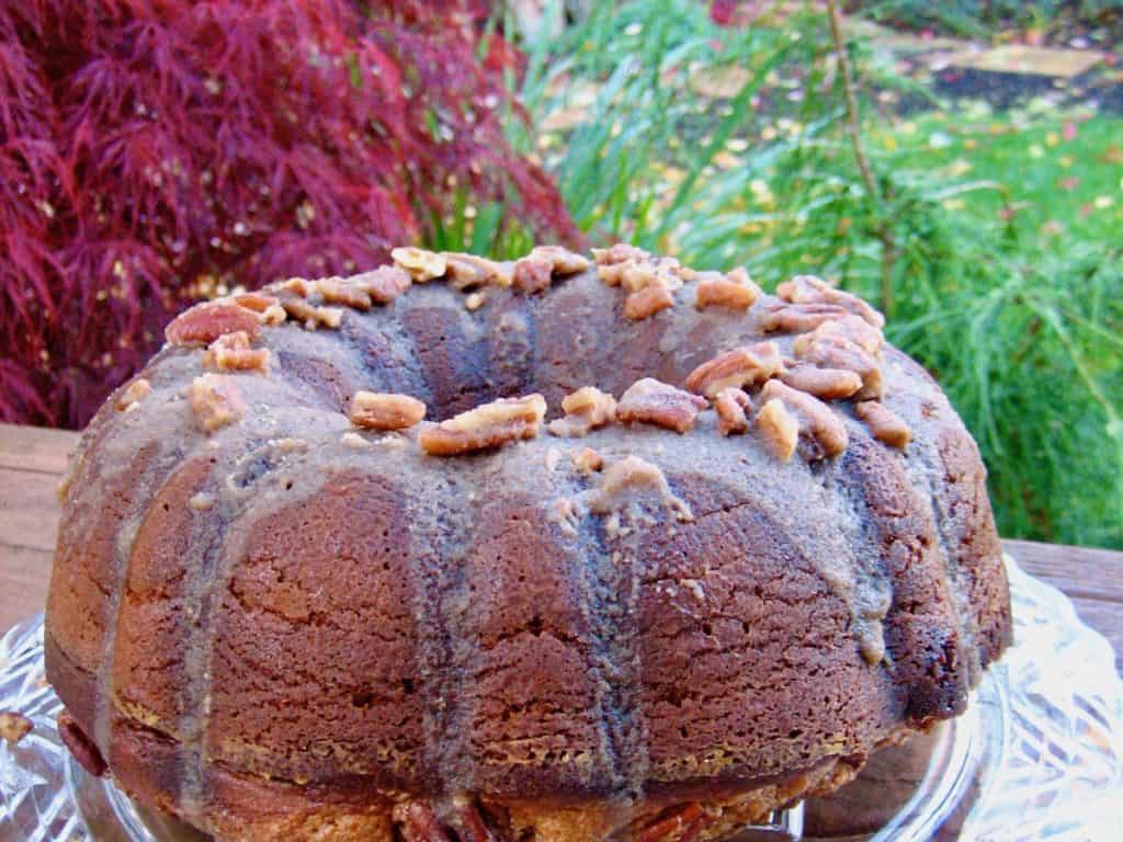 A whole Pecan Praline Cake topped with praline pecans on a crystal plate in the garden.
