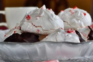 Crisp and chewy Peppermint Meringue Cookies stacked on a plate with a cup of Hot Chocolate in the background.