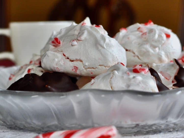 Crisp and chewy Peppermint Meringue Cookies stacked on a plate with a cup of Hot Chocolate in the background.