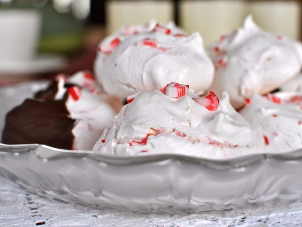 Crisp and chewy Peppermint Meringue Cookies stacked on a plate with a cup of Hot Chocolate in the background.