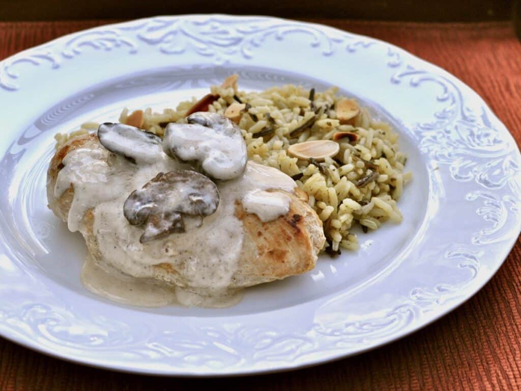 Chicken Breasts with Champagne Sauce is served with a rice pilaf on a white plate.