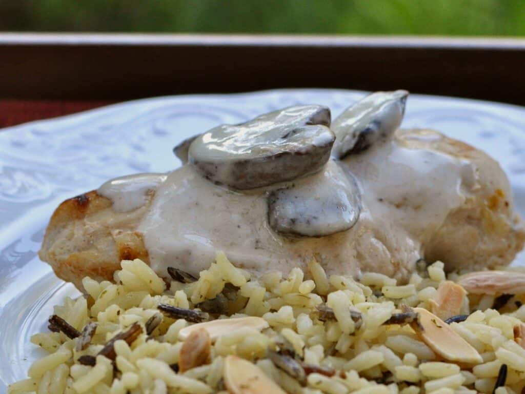 Mushrooms on top of Chicken Breasts with Champagne Sauce is served with a rice pilaf on a white plate.