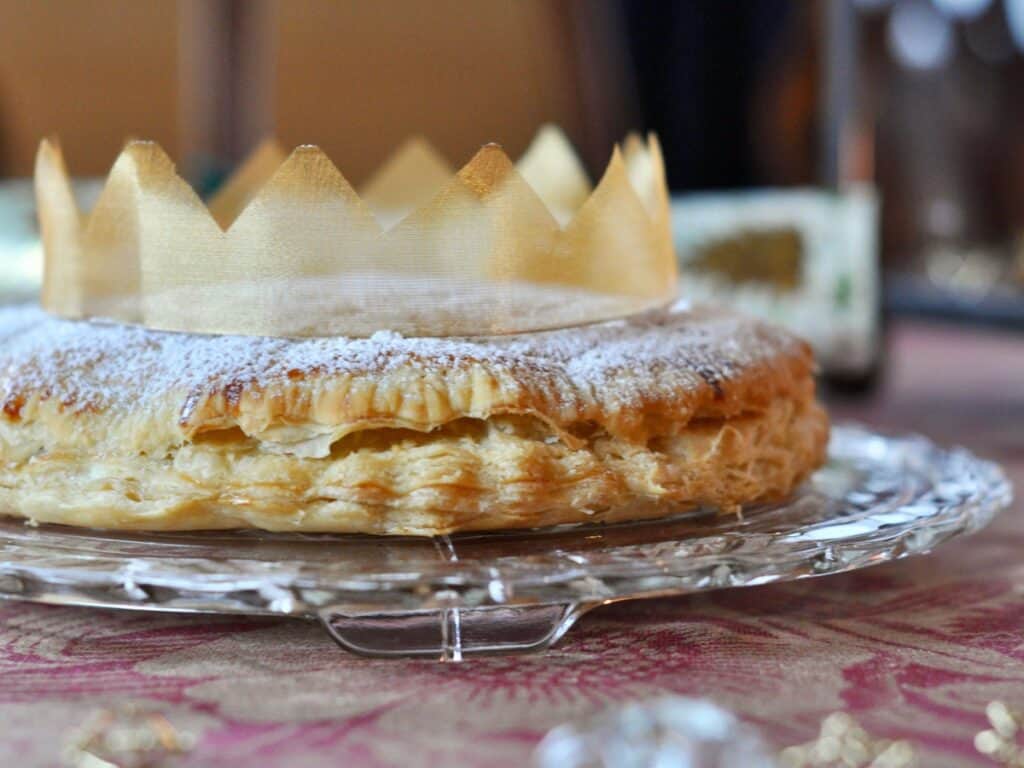 A Galette des Rois, or King Cake, is topped with powdered sugar and adorned with a ribbon crown.
