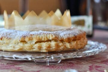 A Galette des Rois, or King Cake, is topped with powdered sugar and adorned with a ribbon crown.