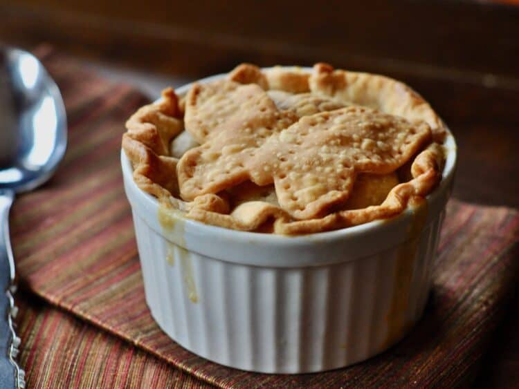 A Homemade Chicken Pot Pie with a pastry crust topped with a pastry butterfly, served with a cloth napkin and serving spoon.