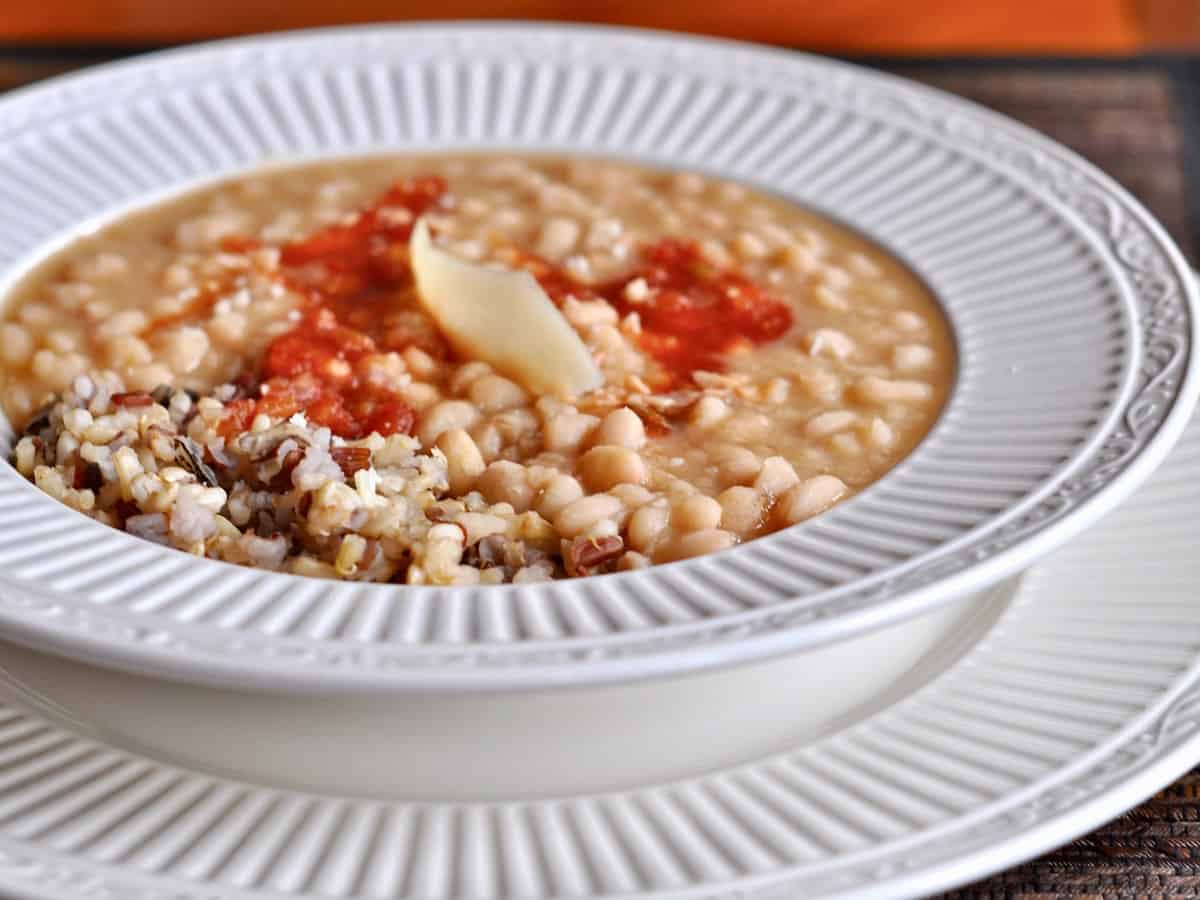 A bowl of Simple White Beans over a rice pilaf with sriracha and Parmesan.