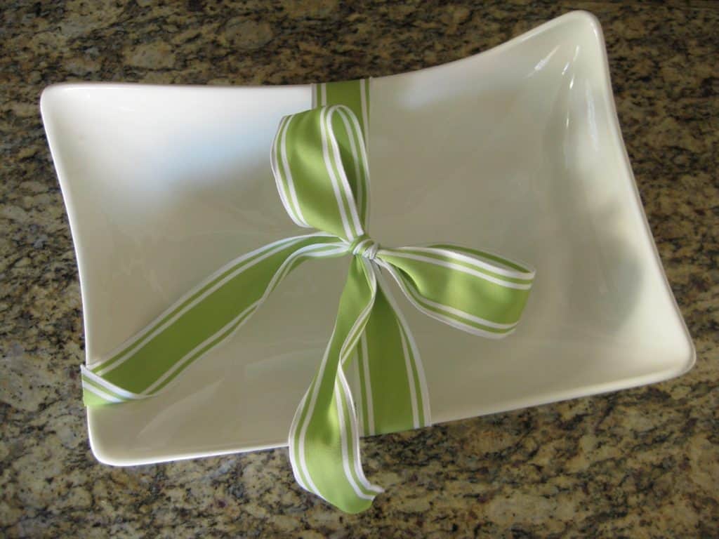 An asymmetrical rectangular white bowl with a green and white ribbon tied around it, displayed on a granite countertop, represents a new beginning.