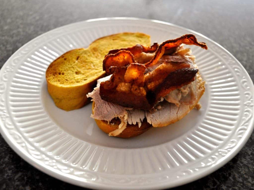 Bacon topped turkey meat on The Best Turkey Sandwich, assembled on a white plate.