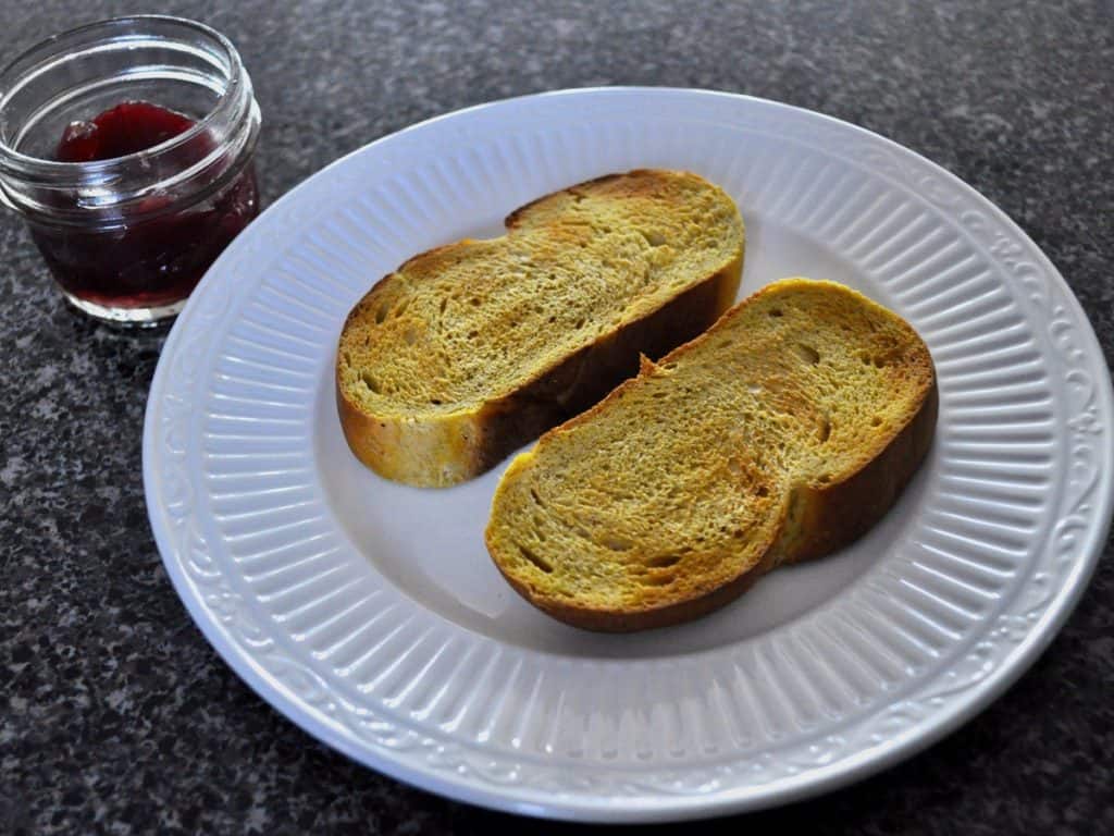 Two slices of toasted Pumpkin Yeast Bread on a white plate beside a jar of Cranberry Sauce.