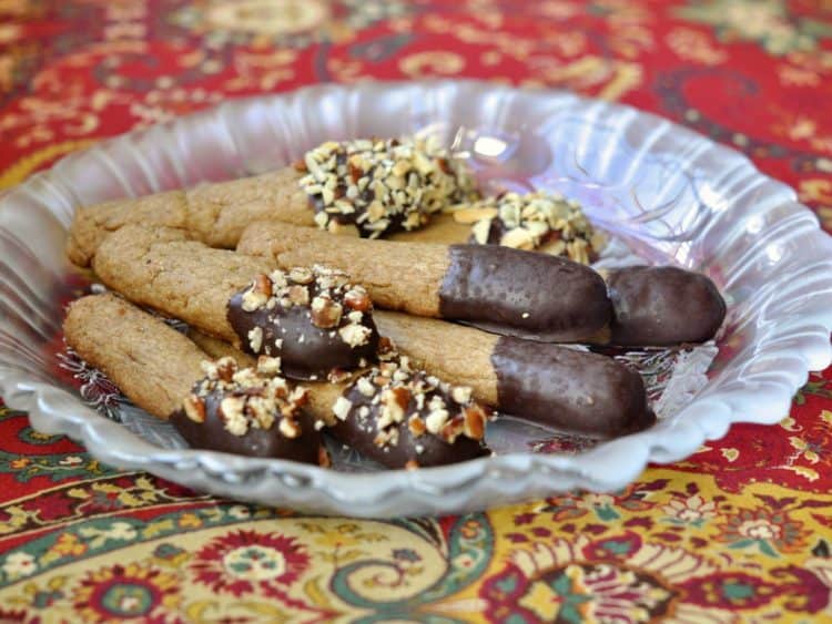 Cappuccino Cookie Sticks piled on a glass plate on an exotic red patterned cloth.