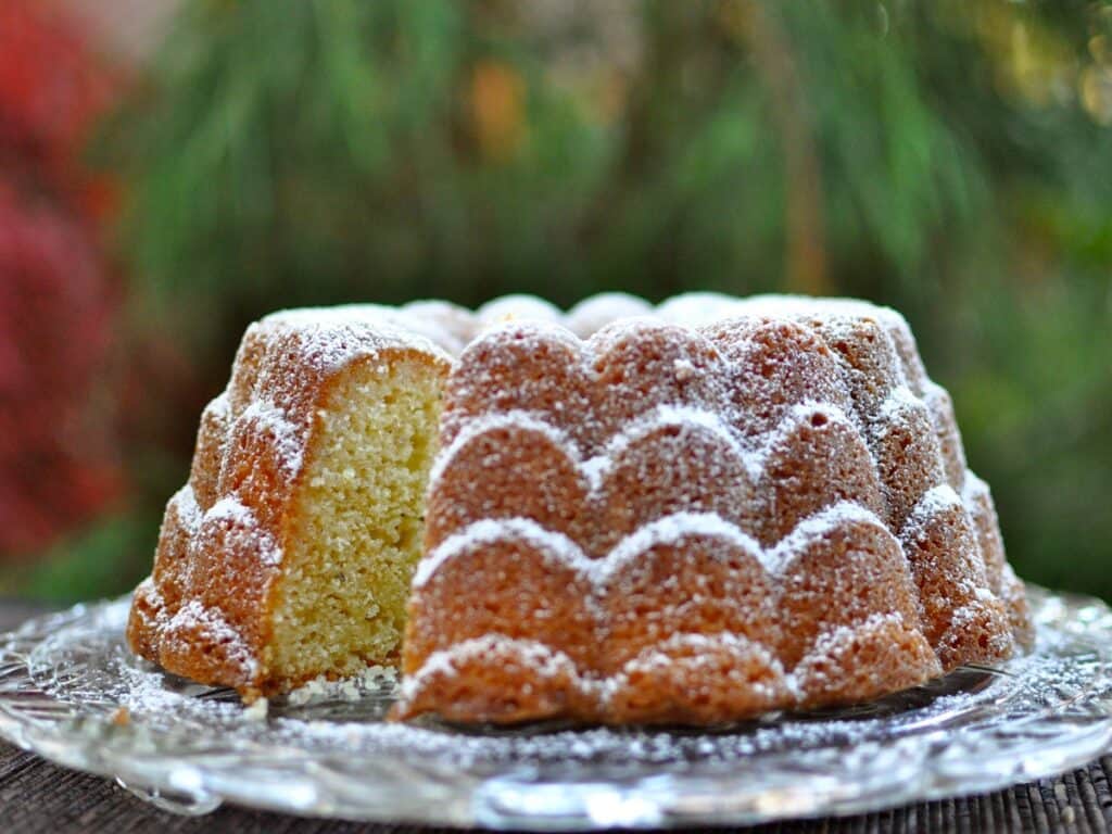 A White Pepper and Ginger Lemon Cake, dusted with powdered sugar, with a slice cutaway to see the inside of the cake. 