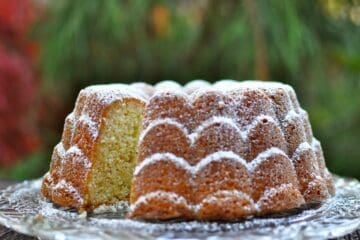 A White Pepper and Ginger Lemon Cake, dusted with powdered sugar, with a slice cutaway to see the inside of the cake.