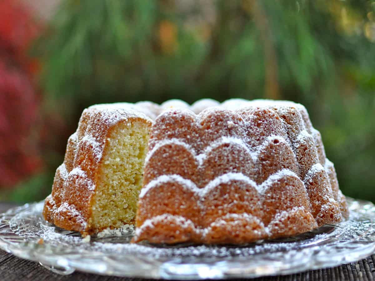 A White Pepper and Ginger Lemon Cake, dusted with powdered sugar, with a slice cutaway to see the inside of the cake.