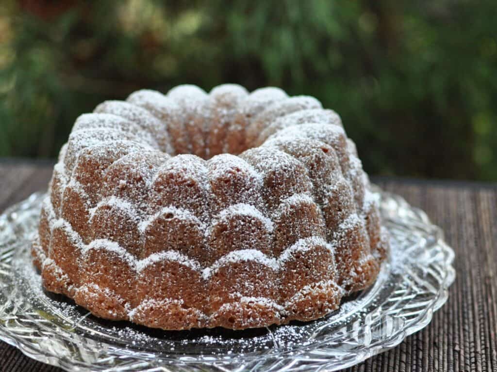 White Pepper and Ginger Lemon Cake dusted with powdered sugar and served on a glass cake plate.