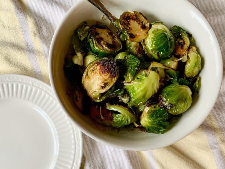 Pan-Roasted Parmesan Sprouts in a serving bowl with spoon, viewed from above.