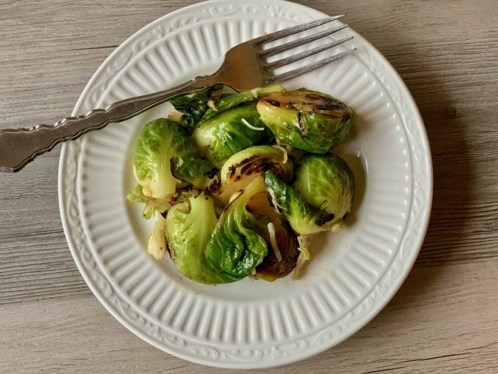 Parmesan Brussels sprouts on a small serving plate with a fork. 