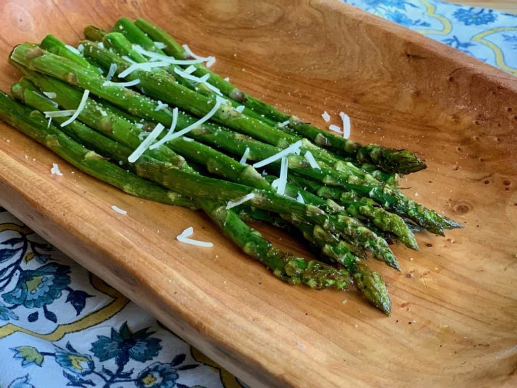 Roasted Asparagus, garnished with a few shreds of parmesan, served on a wooden tray.