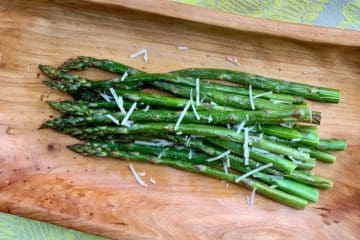 Roasted Asparagus, garnished with a few shreds of parmesan, served on a wooden tray.