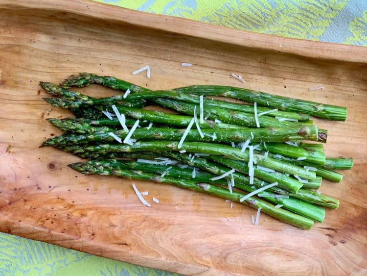 Roasted Asparagus, garnished with a few shreds of parmesan, served on a wooden tray.