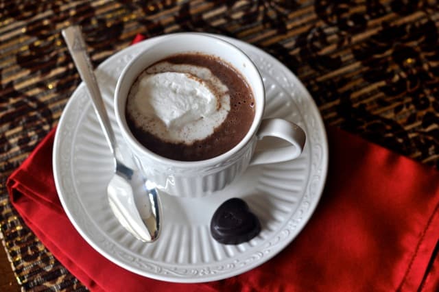 Hot Chocolate topped with whipped cream in a cup and saucer with a chocolate heart on the side