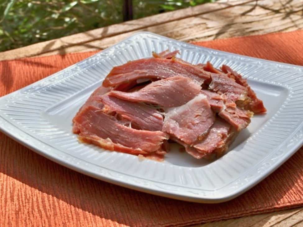 Country ham slices with white flecks are served on a white dinner plate.