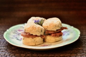 Rosemary Biscuits filled with slivers of country ham, topped with rosemary flowers on an antique plate.