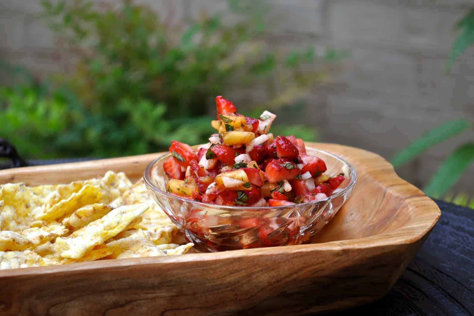 Sweet Strawberry Salsa fills a small glass bowl on a wooden tray served with chips for dipping.