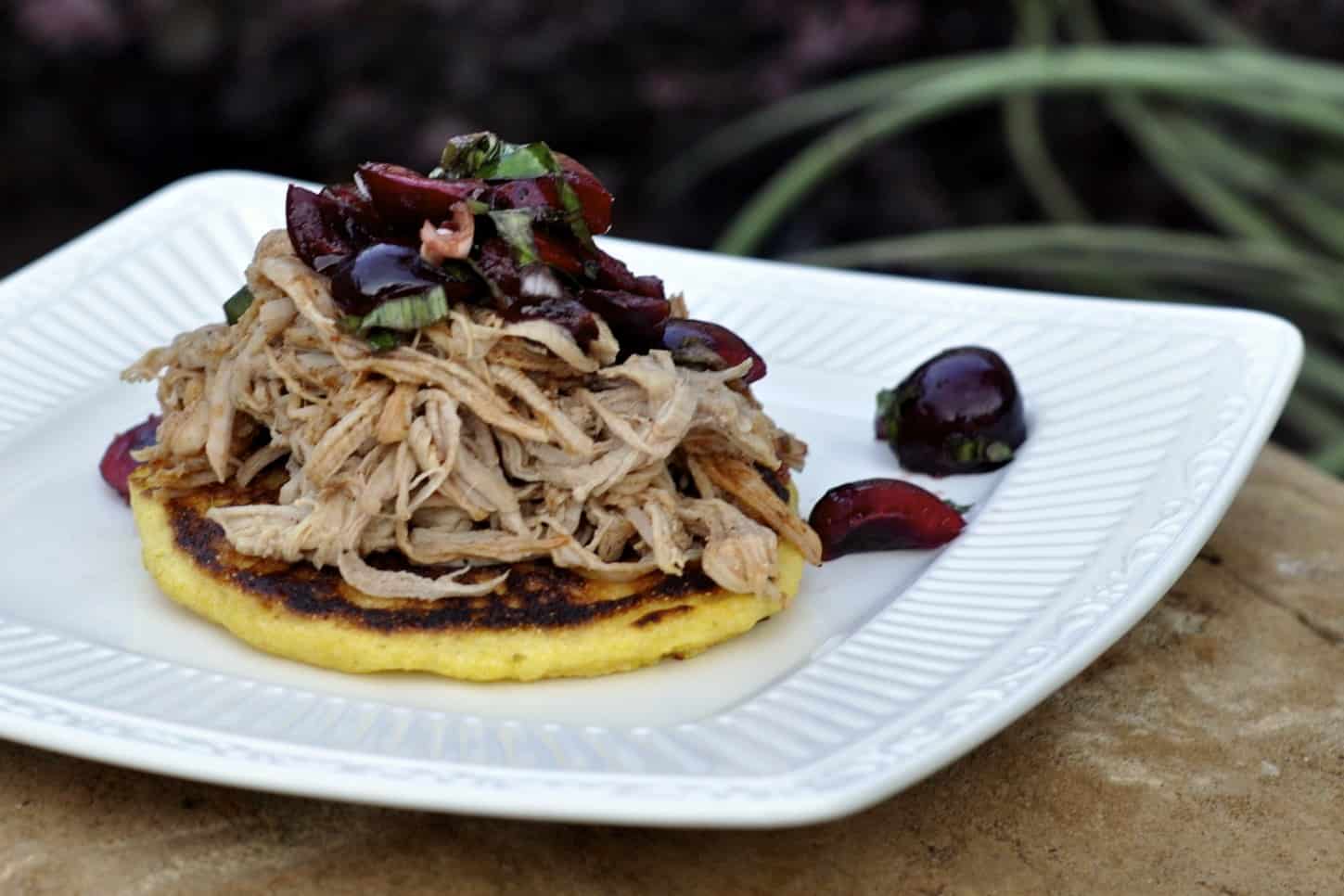 Cornbread Griddle Cakes topped with Pulled Pork Barbecue and Sweet Cherry Salad on a square dinner plate.