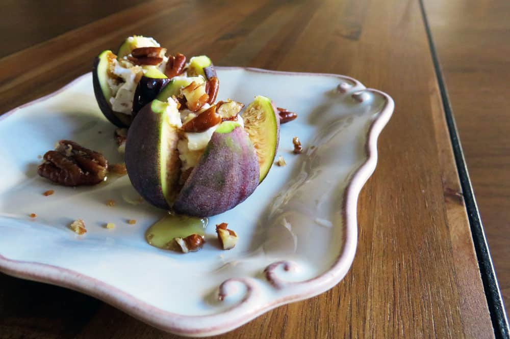 An appetizer or garnish of figs sliced halfway into quarters, then drizzled with honey and topped with a toasted pecan.