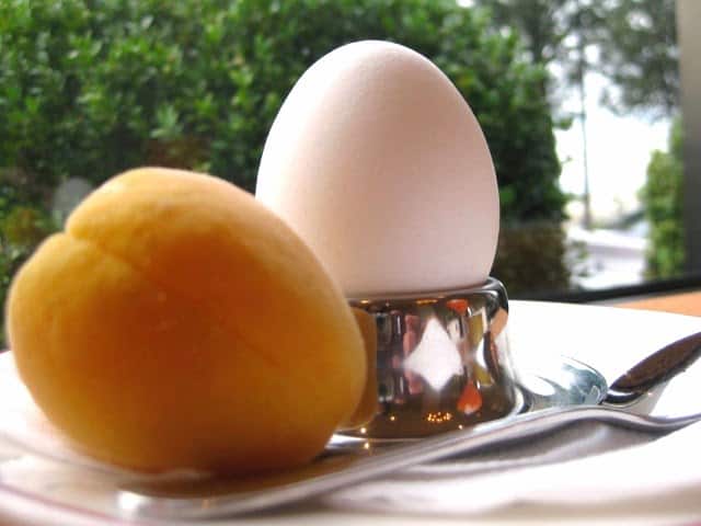 A Soft Boiled Egg on an egg stand beside an apricot and an egg spoon.