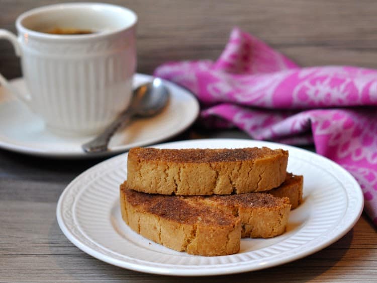 Cinnamon Toast Biscotti stacked on white plate beside a white coffee cup with pink towel.