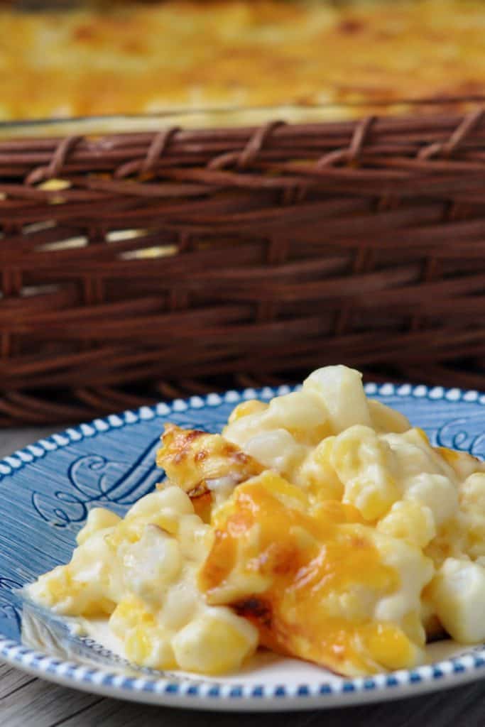 Hominy Au Gratin topped with cheese on Courier and Ives Ironstone plate with basket background