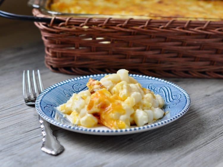 A serving of Hominy Au Gratin Casserole served on a small blue plate beside a serving basket